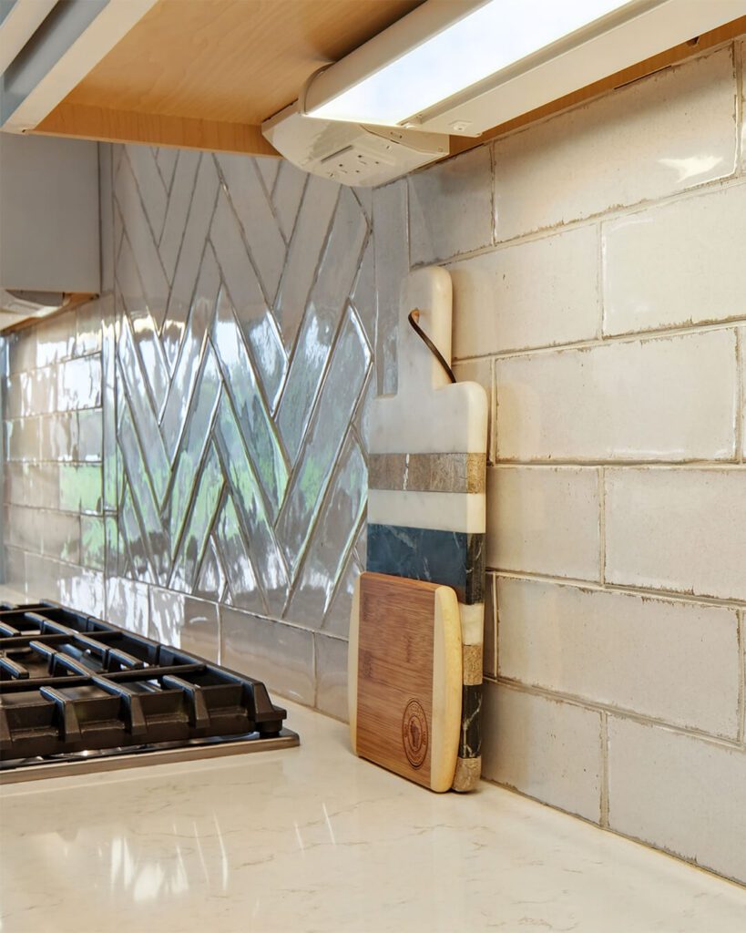 Glossy herringbone backsplash with soft neutral tones, professionally installed behind the cooktop by Esox Custom Tiling in Madison, WI—adds elegant movement and depth to contemporary kitchens.