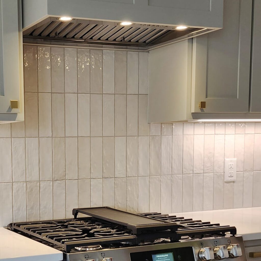 Light neutral vertical stacked backsplash tiles with gentle surface variation, enhancing the sense of height and simplicity in a compact kitchen.
