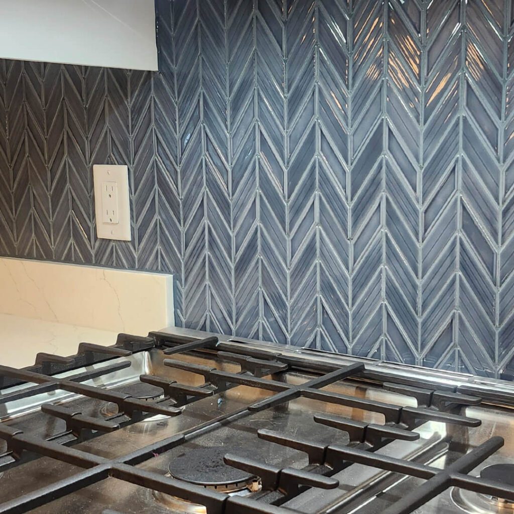 Sophisticated navy herringbone backsplash behind the stovetop, offering bold texture and a refined focal point in a transitional or modern kitchen.